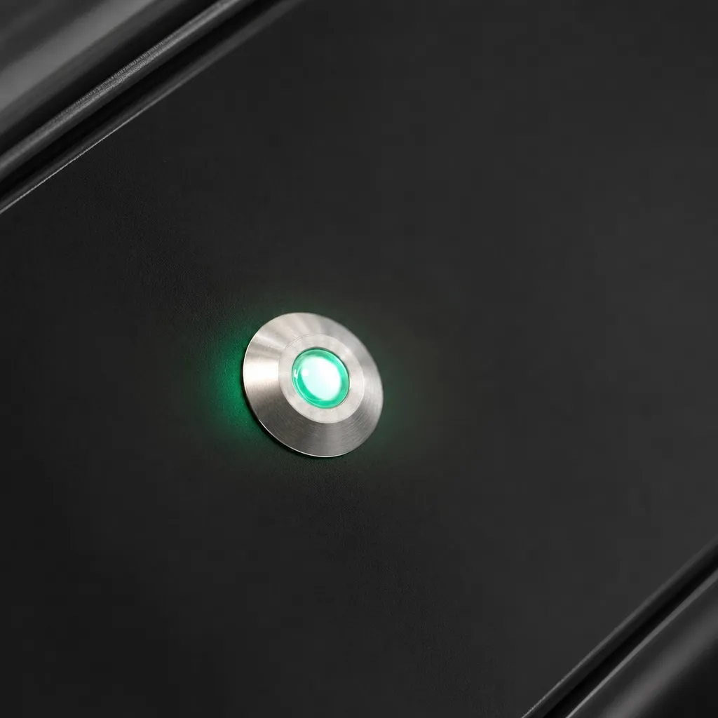 Close view of a small indicator lamp set in a nickel collar, lit mint against a dark panel.